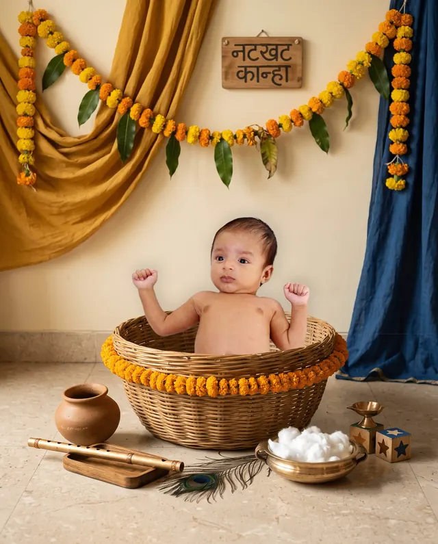 Baby peeking from a woven basket beneath mustard and blue drapes and marigold garlands
