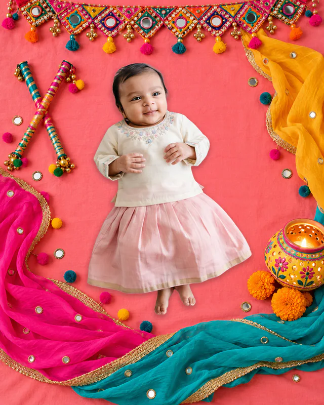 Baby on a bright pink Garba backdrop with dandiya sticks, mirrorwork drapes and a decorated festive pot