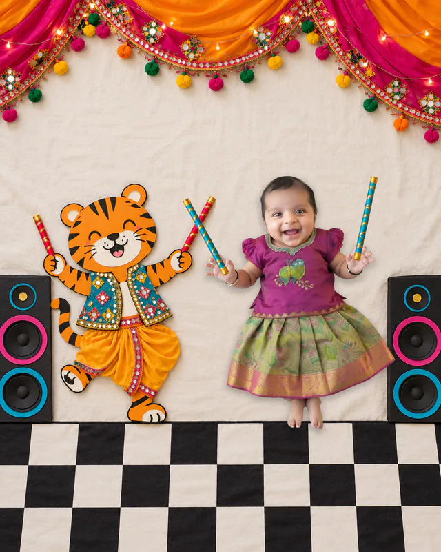 Baby and a cartoon tiger dancing with dandiya sticks on a checkered floor beneath colourful festive drapes