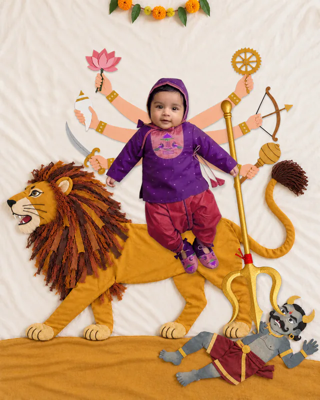 Baby in a Maa Durga-inspired portrait with a fabric lion, lotus flowers, illustrated goddess arms and a small demon figure