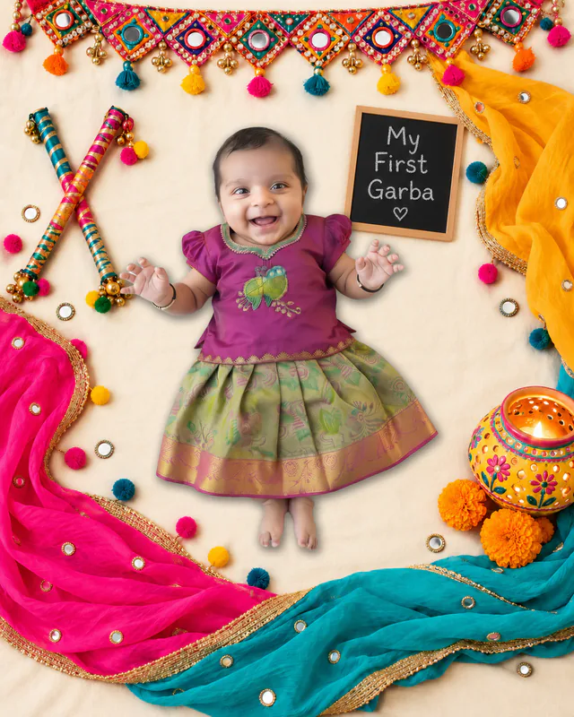 Baby beside a My First Garba chalkboard, crossed dandiya sticks, colourful drapes and a decorated pot