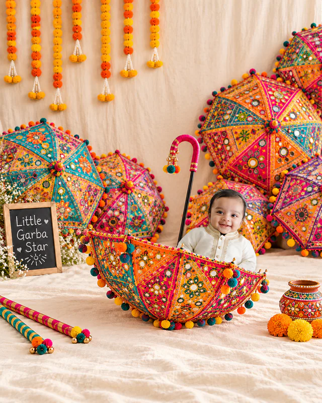 Smiling baby sitting in an embroidered umbrella with colourful umbrellas, marigold garlands and a Little Garba Star sign