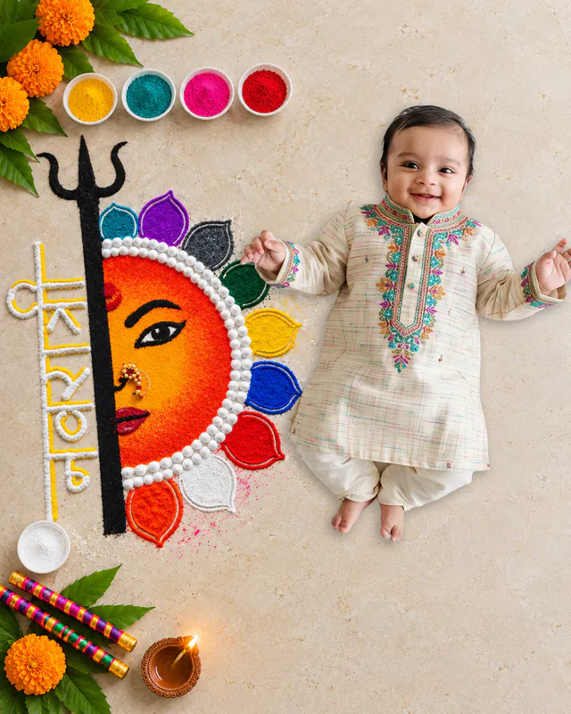 Baby beside a colourful Devi face rangoli with a trishul, bowls of colour, marigolds, dandiya sticks and a diya